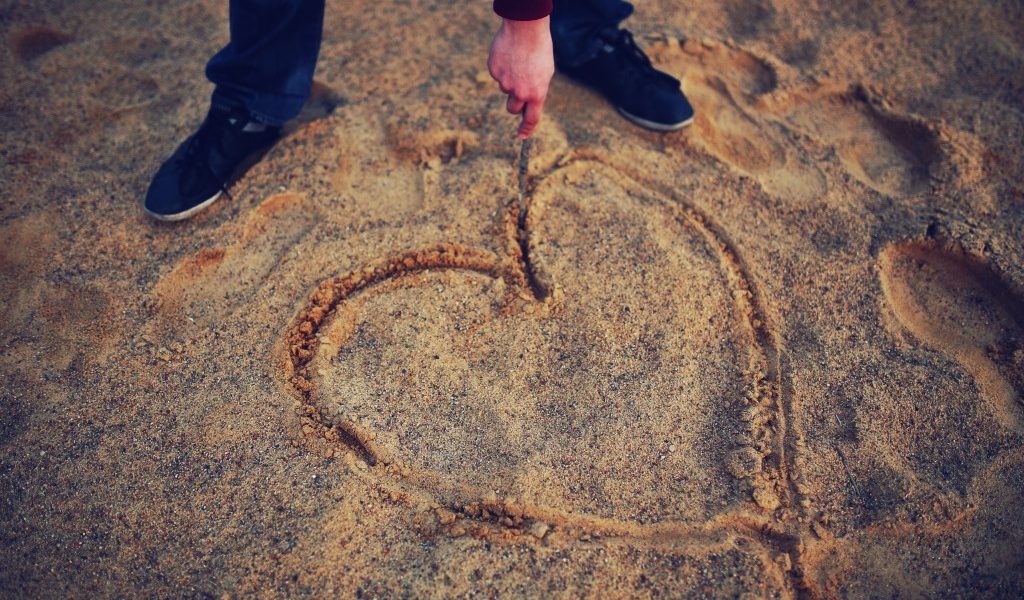 person drawing heart symbol on beach