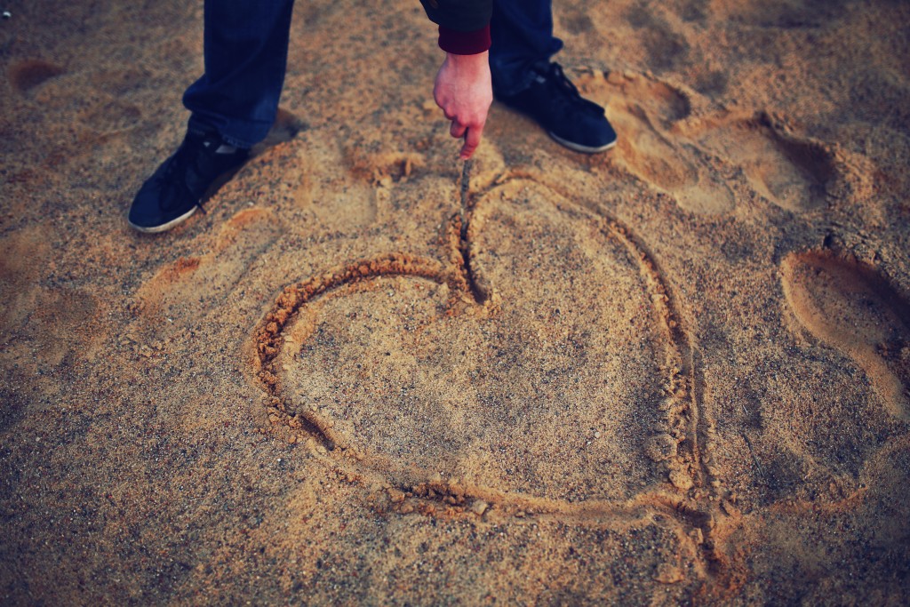 person drawing heart symbol on beach